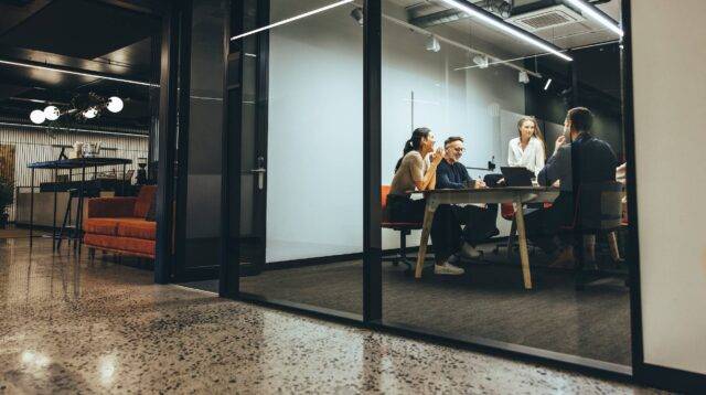 Business colleagues having a meeting in a transparent boardroom. Group of happy business professionals having a discussion during a briefing. Diverse businesspeople collaborating on a new project.