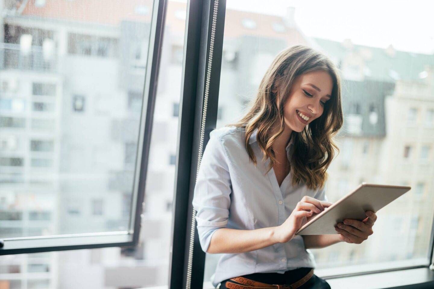 Young businesswoman using a digital tablet while standing in front of windows in office