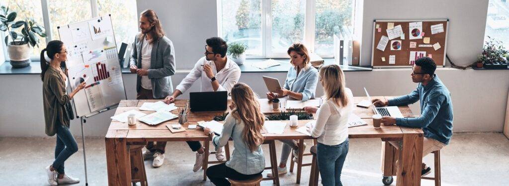 A group of diverse colleagues in an office setting watching a presentation